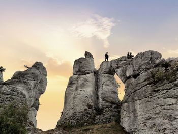 People on rock formation against sky during sunset