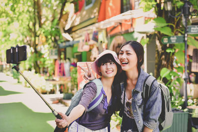 Happy friends taking selfie while standing on footpath