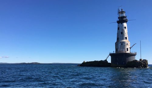 Lighthouse by sea against clear blue sky