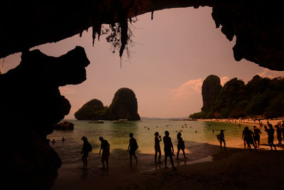 Silhouette people enjoying at beach seen through cave