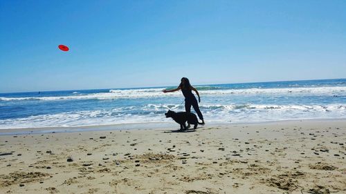 Woman playing with dog on beach against sky