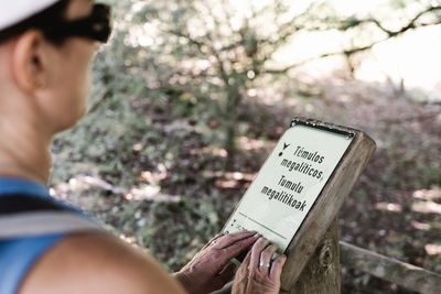 From above anonymous blind elderly traveler touching and reading braille on signboard while visiting park on summer weekend day