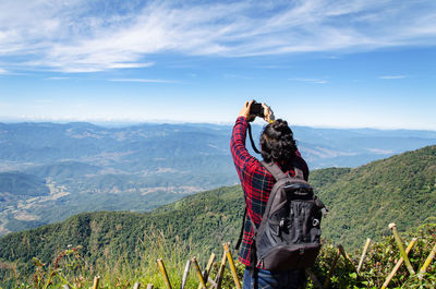 Rear view of man photographing while standing on mountain against cloudy sky