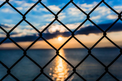 Scenic view of sea seen through chainlink fence during sunset