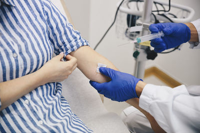 Cropped hands of doctor injecting female patient on arm in hospital