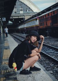 Portrait of woman crouching at railroad station platform in city