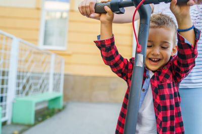 Midsection of mother standing by cheerful son playing with push scooter