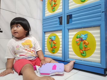 Full length of cute girl holding toy while sitting on sofa