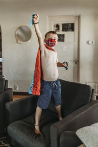 Young boy dressed as super hero standing on couch with mask on