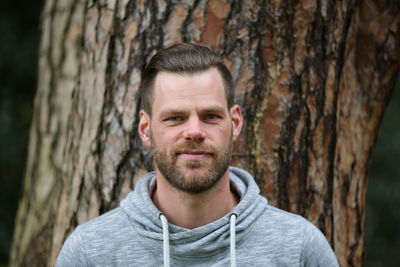 Portrait of smiling young man against tree trunk