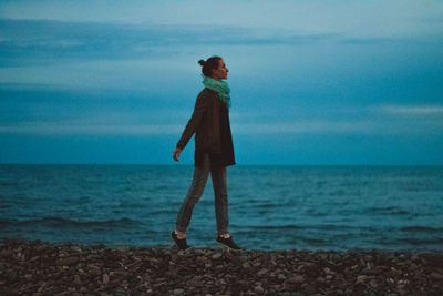 Rear view of young woman standing at beach against sky