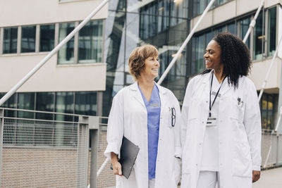 Happy female doctors looking at each other while standing in front of hospital