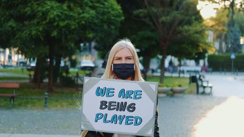 Portrait of woman wearing mask with banner standing on road