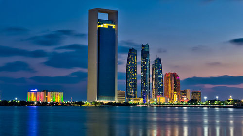 Illuminated modern buildings in city against sky at night