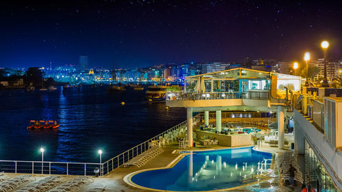 High angle view of illuminated bridge over river by buildings at night