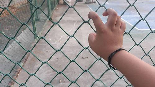 Cropped image of hand holding chainlink fence