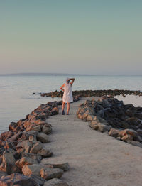 Woman standing on rock at beach against sky