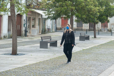 Full length of woman wearing mask walking on footpath in city