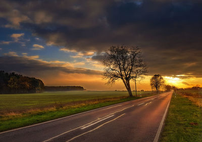 Road by trees against sky during sunset