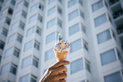 Hand holding ice cream cone against modern building