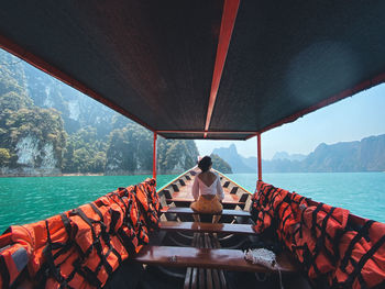 Rear view of woman sitting on boat in sea against sky