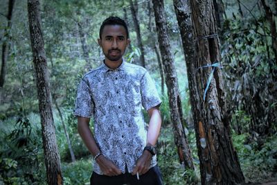 Portrait of young man standing against trees in forest