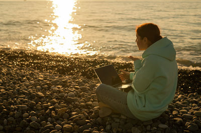 Rear view of woman using mobile phone at beach