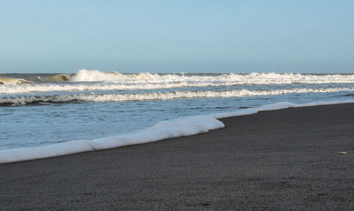 Waves rushing towards shore against sky