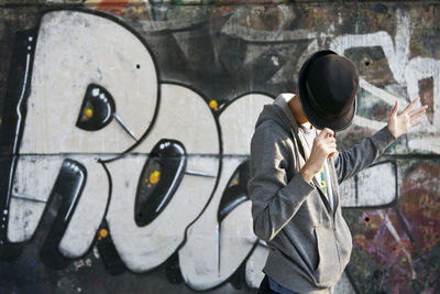 Side view of man standing against graffiti wall