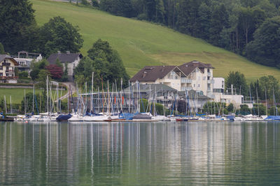 Sailboats in lake by houses against trees and mountain