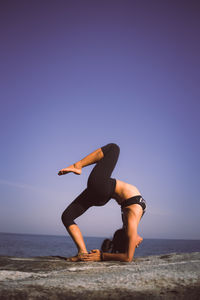 Woman practicing yoga at beach against sky