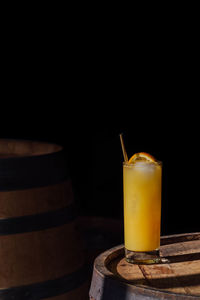 Orange juice drink in tall glass with gold straw, sitting on whiskey barrel in the sunlight