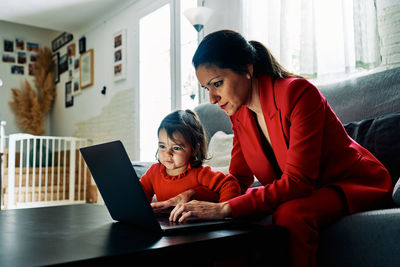 Young executive woman working from home while taking care of her young daughter