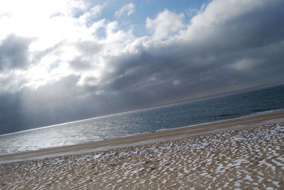 View of calm beach against cloudy sky