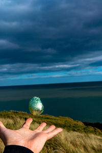 Person holding ball in sea against sky