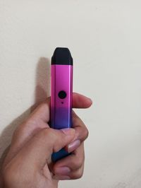 Close-up of hand holding e-cigarette vape against wall