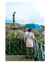 Rear view of man standing on railing during rainy season