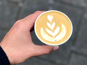Cropped hand of man holding cappuccino with froth art