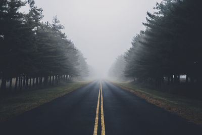 Empty road amidst trees against sky during foggy weather
