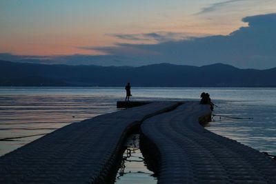 Silhouette people on lake against sky during sunset