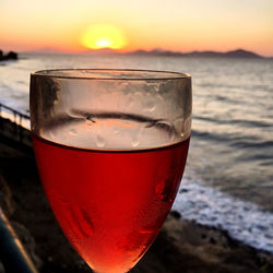 Close-up of beer glass against sea during sunset