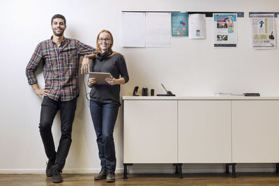 Full length portrait of smiling business colleagues standing by sideboard in creative office