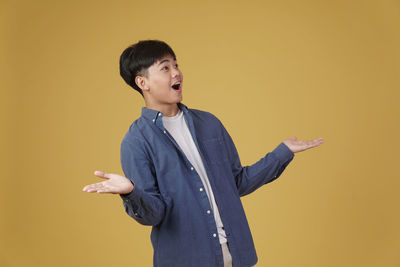 Young man looking away while standing against yellow background