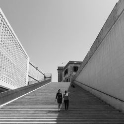 Rear view of people walking on road against clear sky