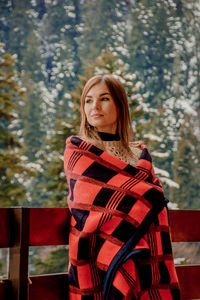 Portrait of young woman sitting on seat against trees