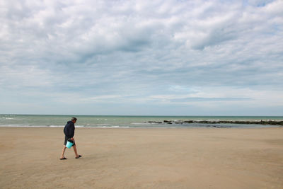 Rear view of man walking at beach against sky