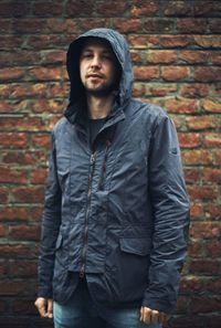 Portrait of young man standing against brick wall