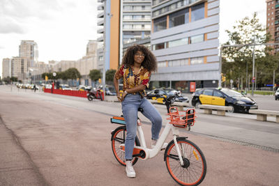 Smiling young woman sitting on bicycle at footpath