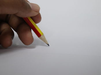 Close-up of hand holding pencils against white background