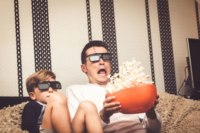 Father with son watching tv while sitting against wall at home